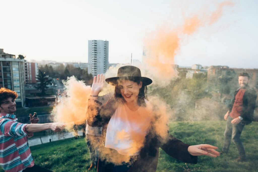 Group of friends on roof, holding colourful smoke flares, young woman walking through orange smoke